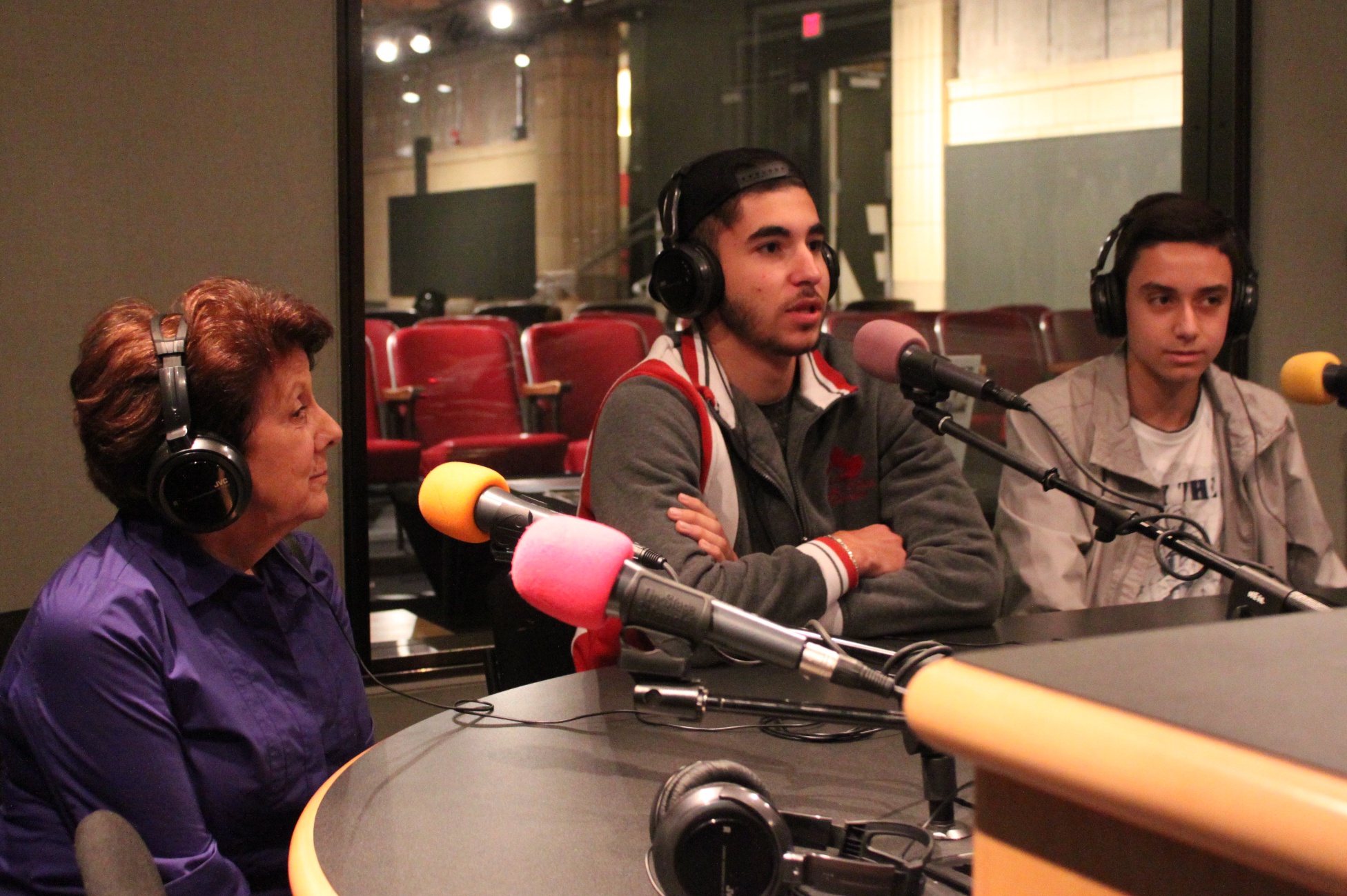 Two teens and an adult wearing headphones speaking into microphones in a radio studio