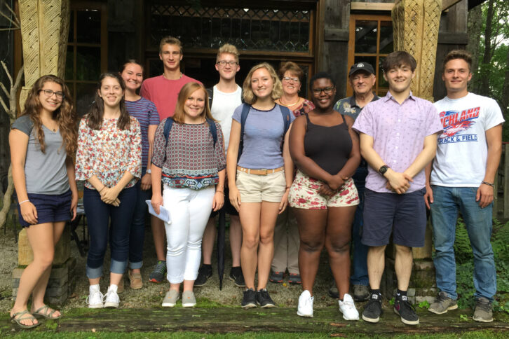 Twelve teens smiling and posing in front of a building