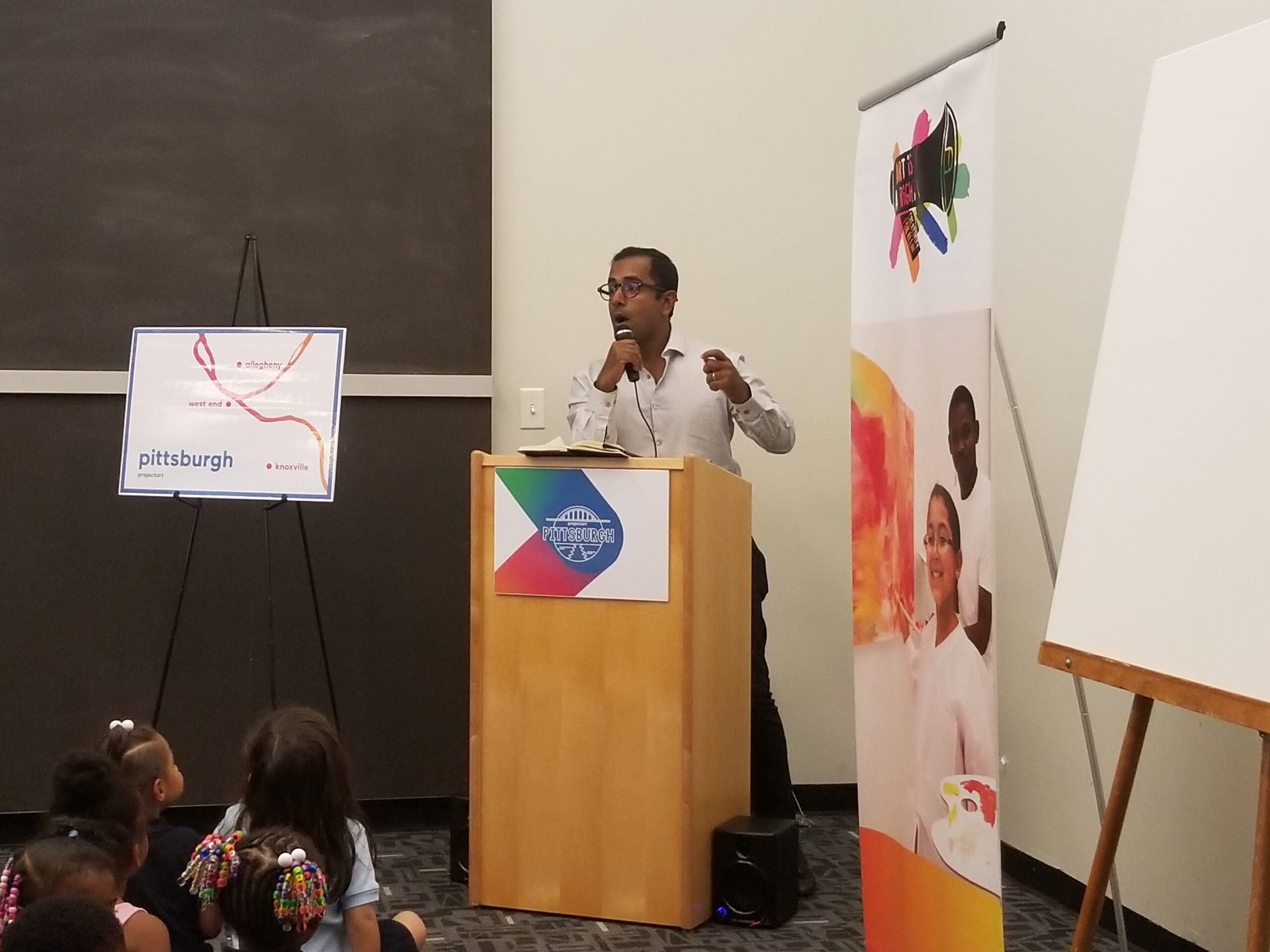 An adult presenting behind a wooden podium next to banners and a graph