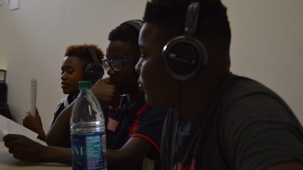 Three youth wearing headphones looking at pieces of paper