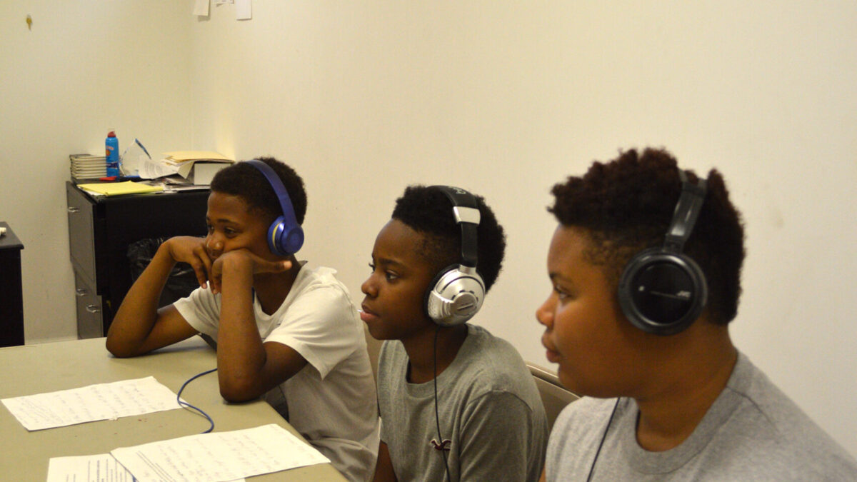 Three youth wearing headphones sitting behind a portable recorder