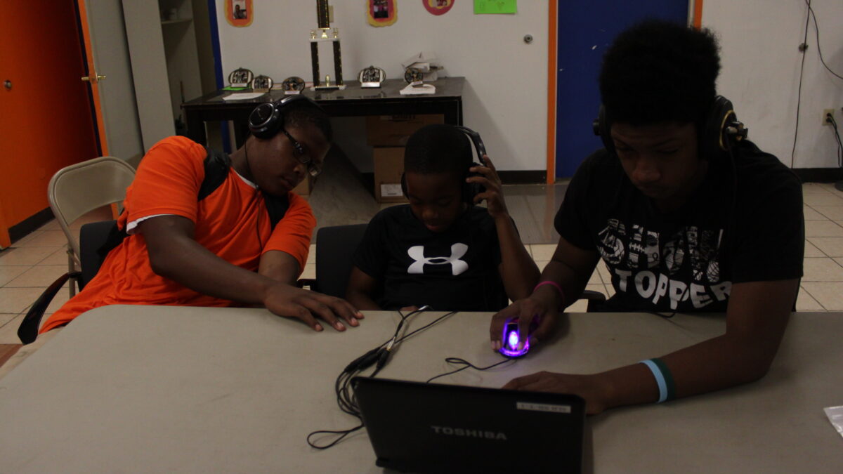 Three youth wearing headphones looking at a laptop computer