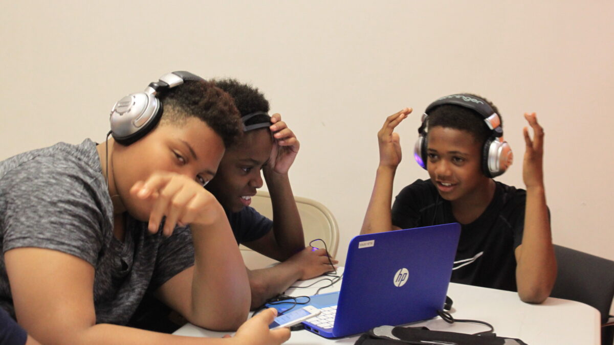 Three youth wearing headphones looking at a laptop computer
