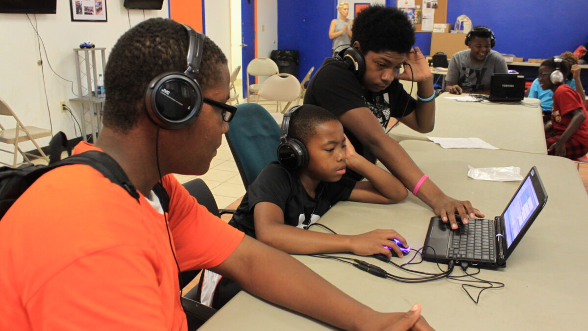 Five youth wearing headphones looking at laptop computers