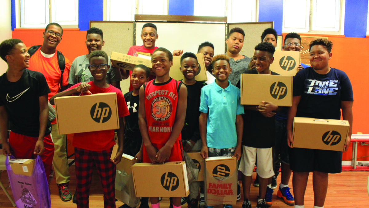 Fifteen youth smiling and holding up laptop computers in boxes