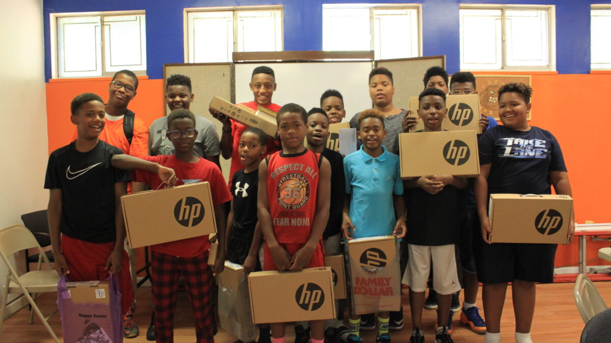 Fifteen youth smiling and holding up laptop computers in boxes