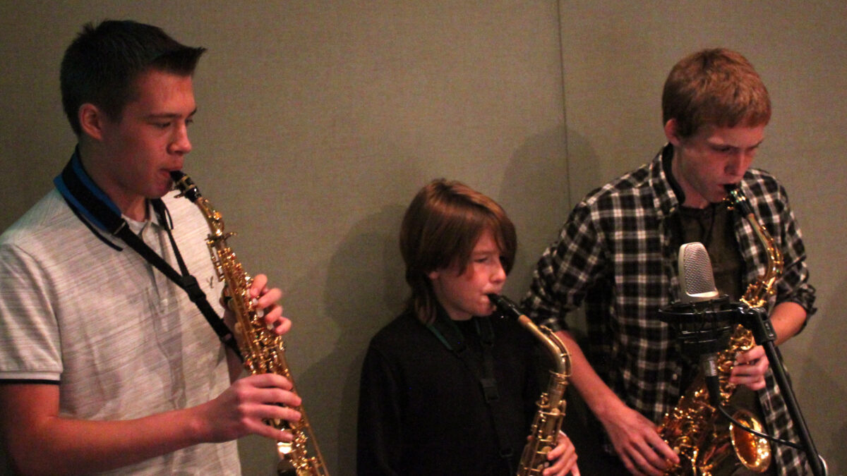 A teen playing soprano saxophone and two youth playing alto saxophones in a radio studio