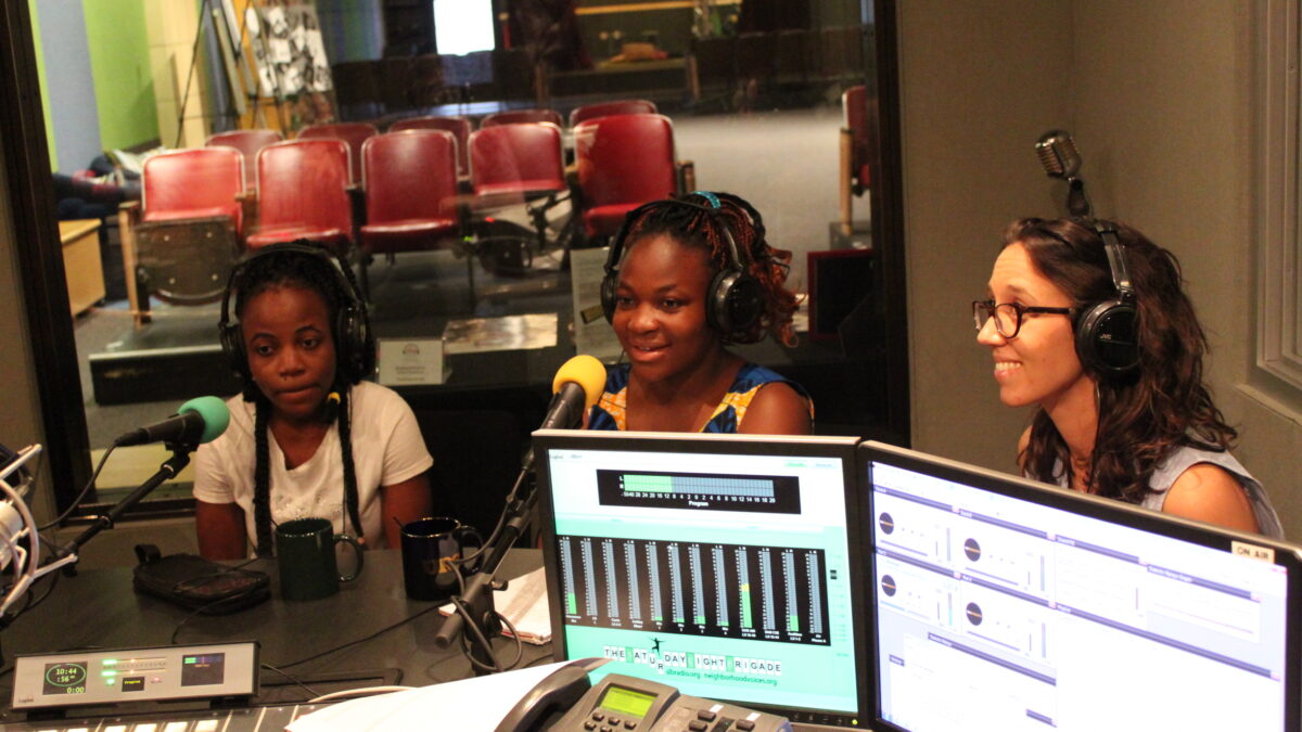 Three teens wearing headphones speaking into microphones in a radio studio