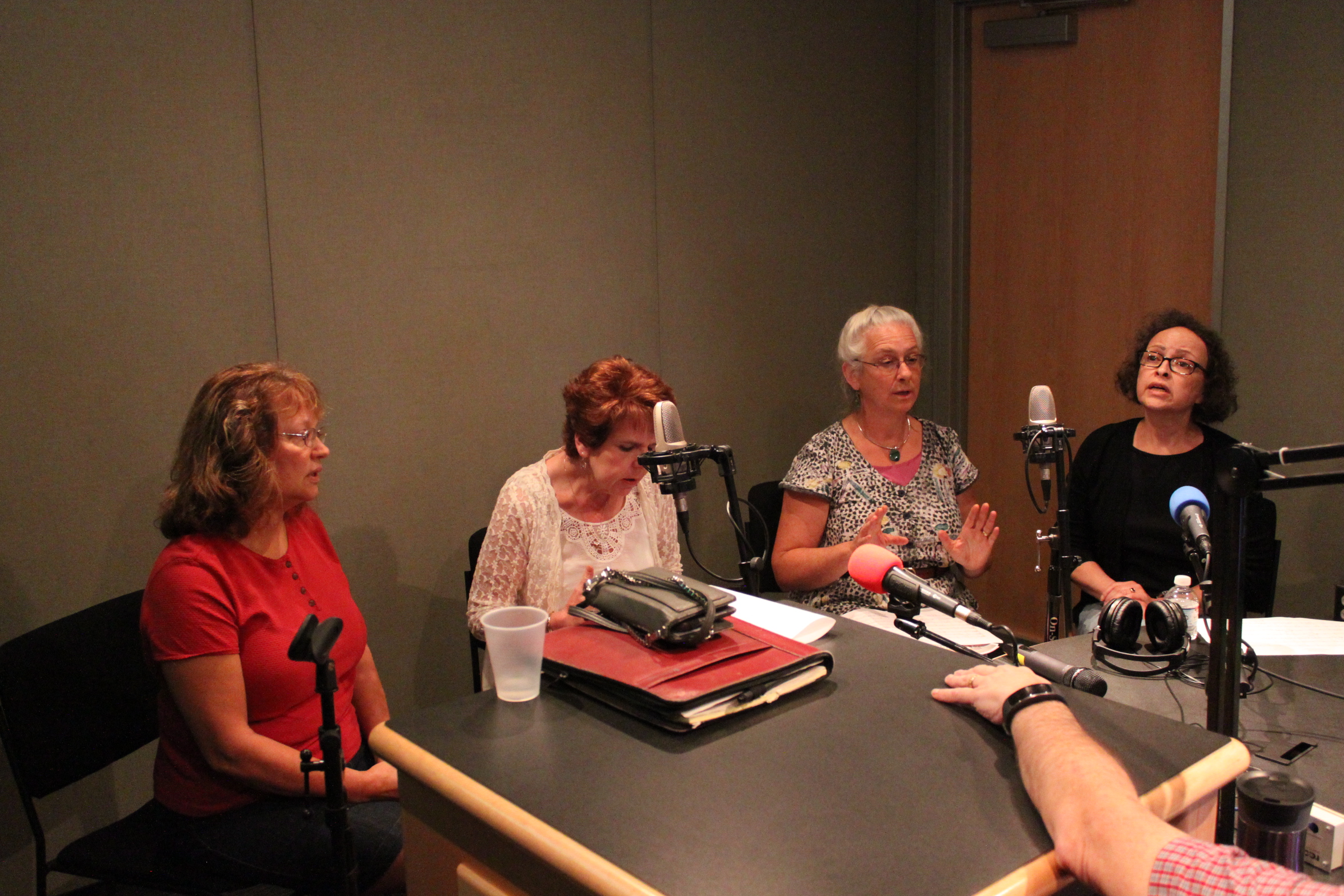 Four adults singing into microphones in a radio studio