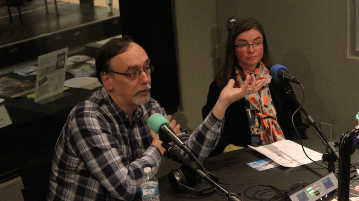 Two adults speaking into microphones in a radio studio