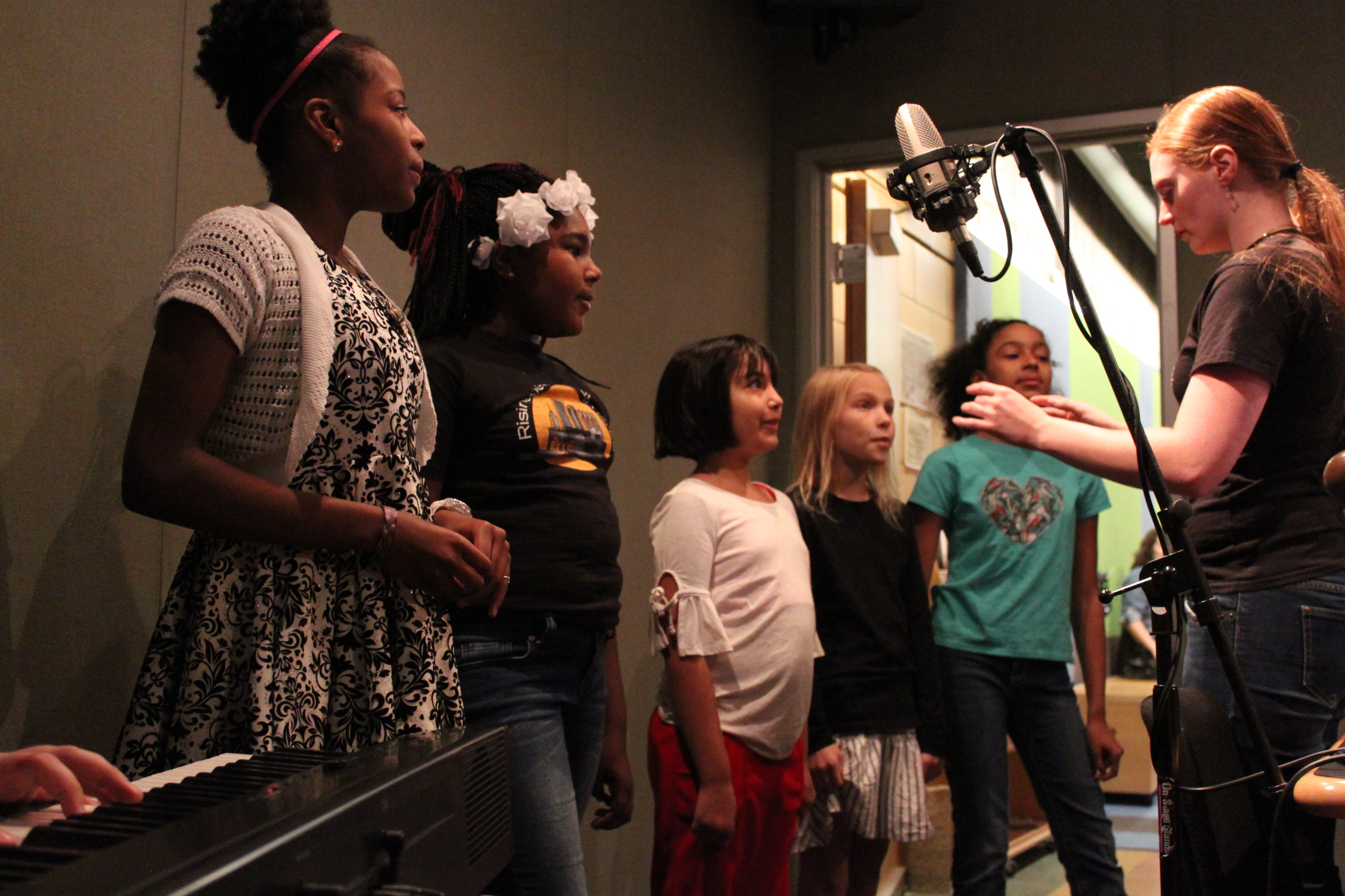 An adult leading a group of five youth in a choir in a radio studio