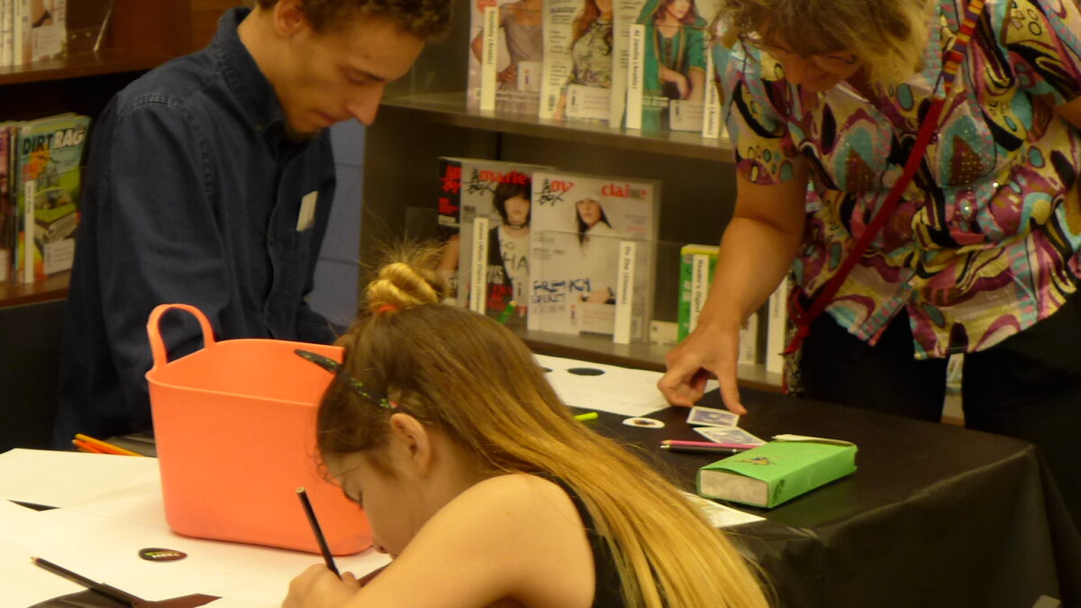 Three teens writing on pieces of paper on a wooden desk in a library