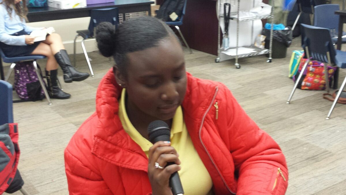 A youth holding and speaking into a microphone in a classroom