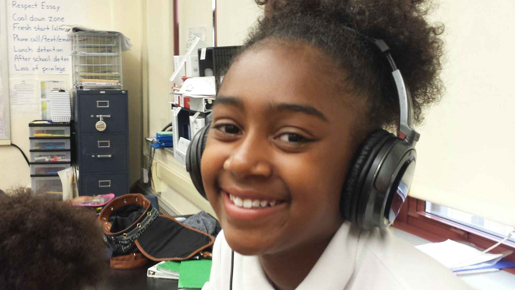 A youth wearing headphones smiling at the camera in a classroom
