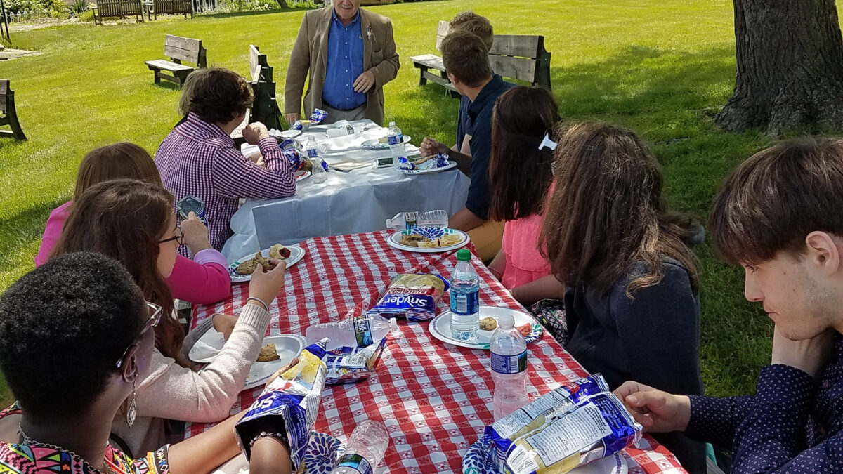 Ten individuals sitting around a picni table in a large green field