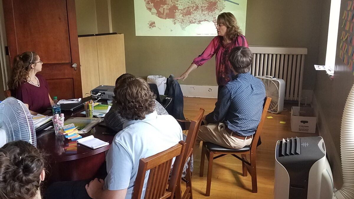 Four teens looking at an adult presenting with a map of the United States behind them
