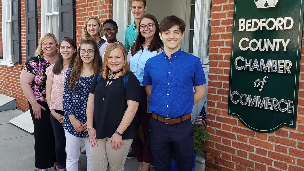 Nine teens smiling and posing in front of the Bedford County Chamber of Commerce
