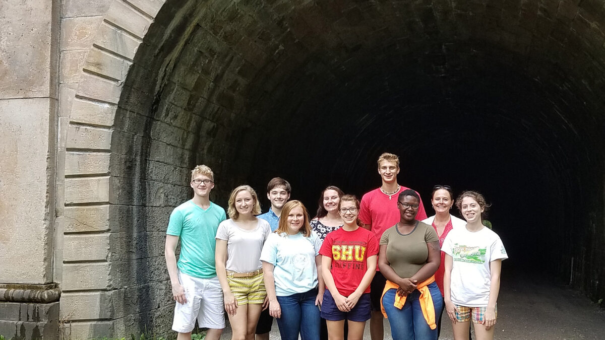 Ten teens posing in front of a tunnel