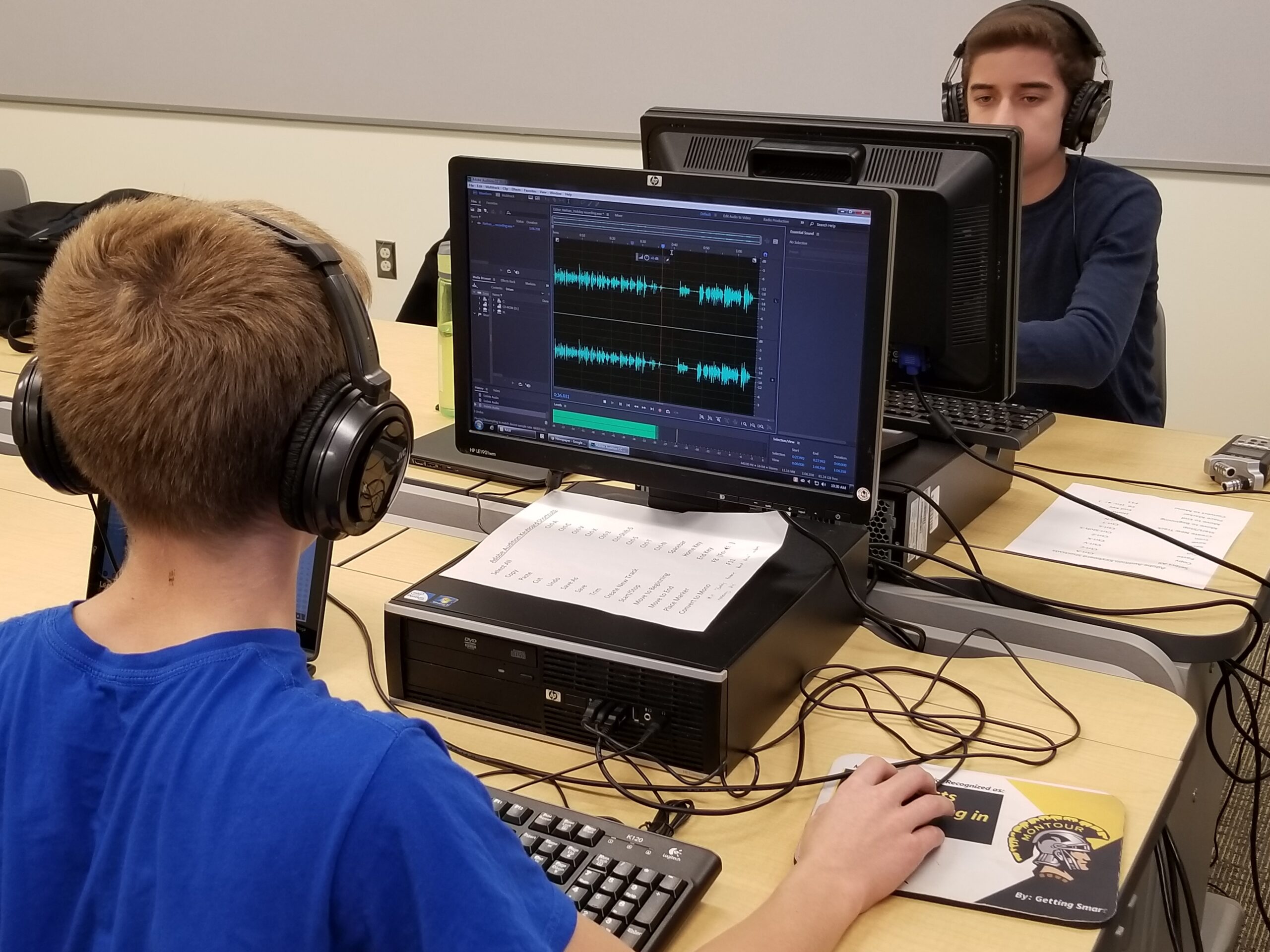 Two youth wearing headphones looking at audio editing software on computers
