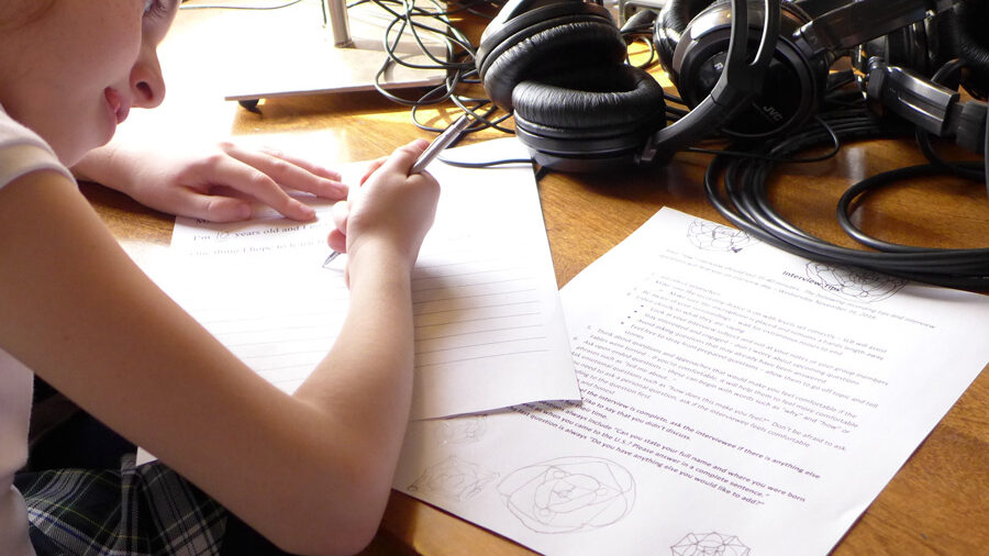 A youth writing on a piece of paper sitting behind a pair of headphones