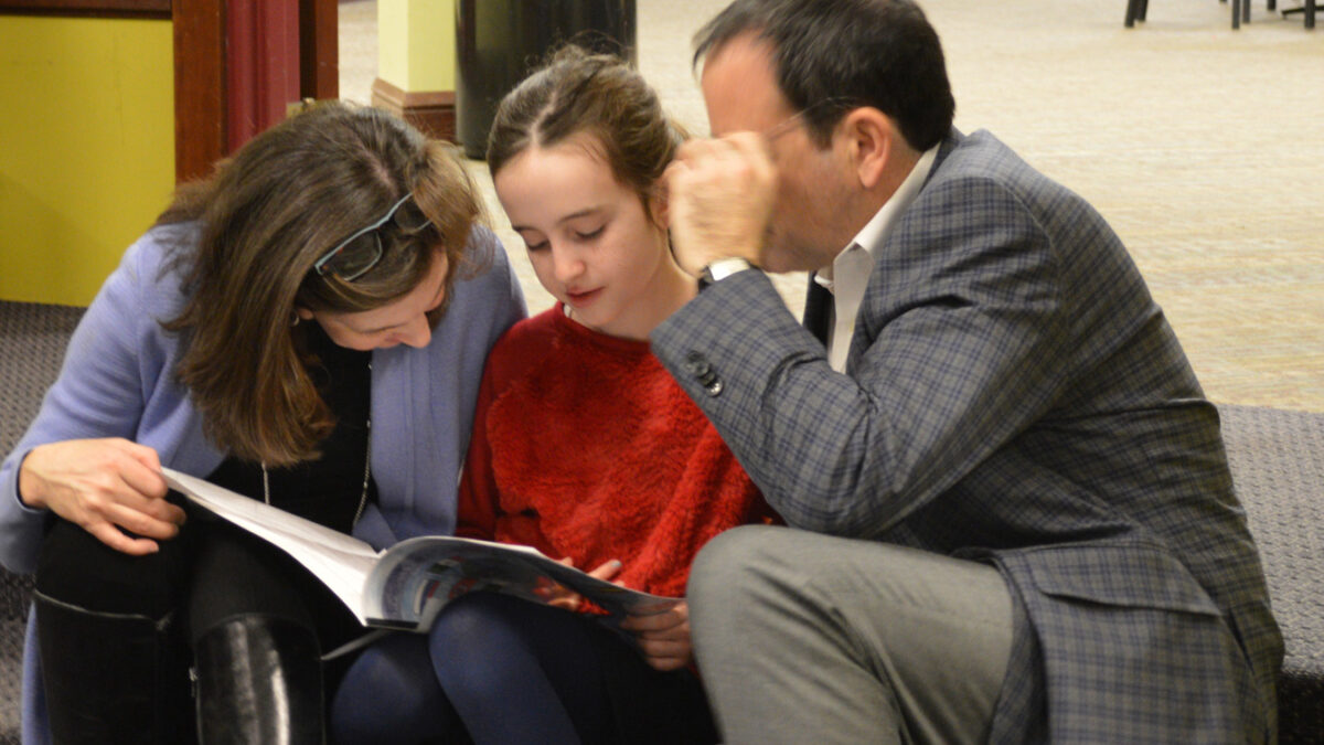 Two adults and a youth looking down at a booklet