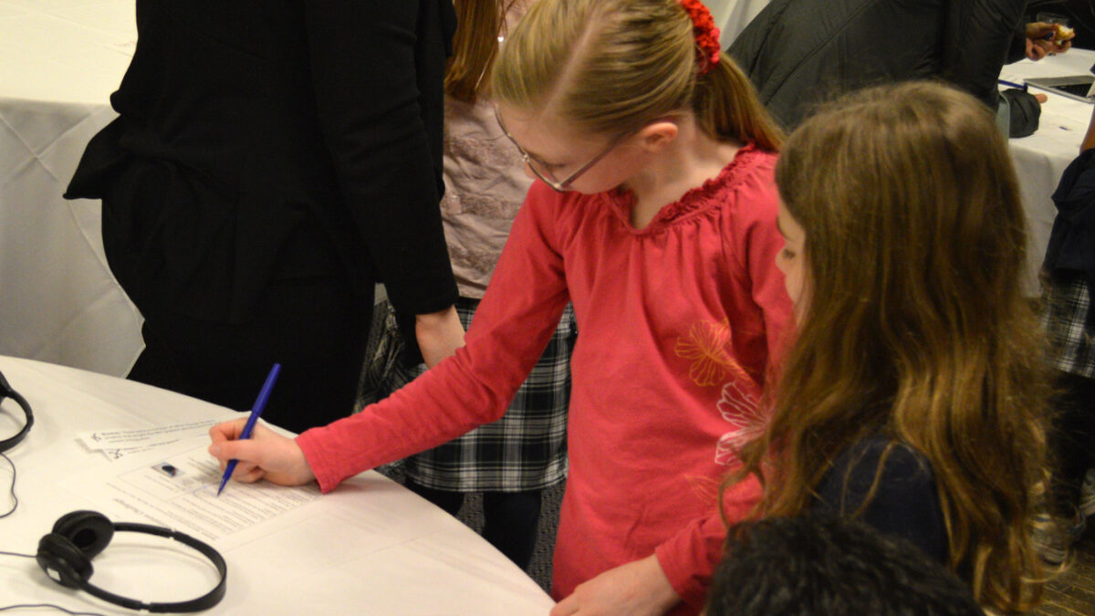 Two youth looking down at a table, one writing on a piece of paper