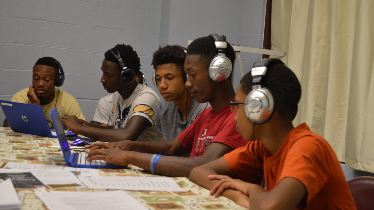 Five youth wearing headphones looking at laptop computers