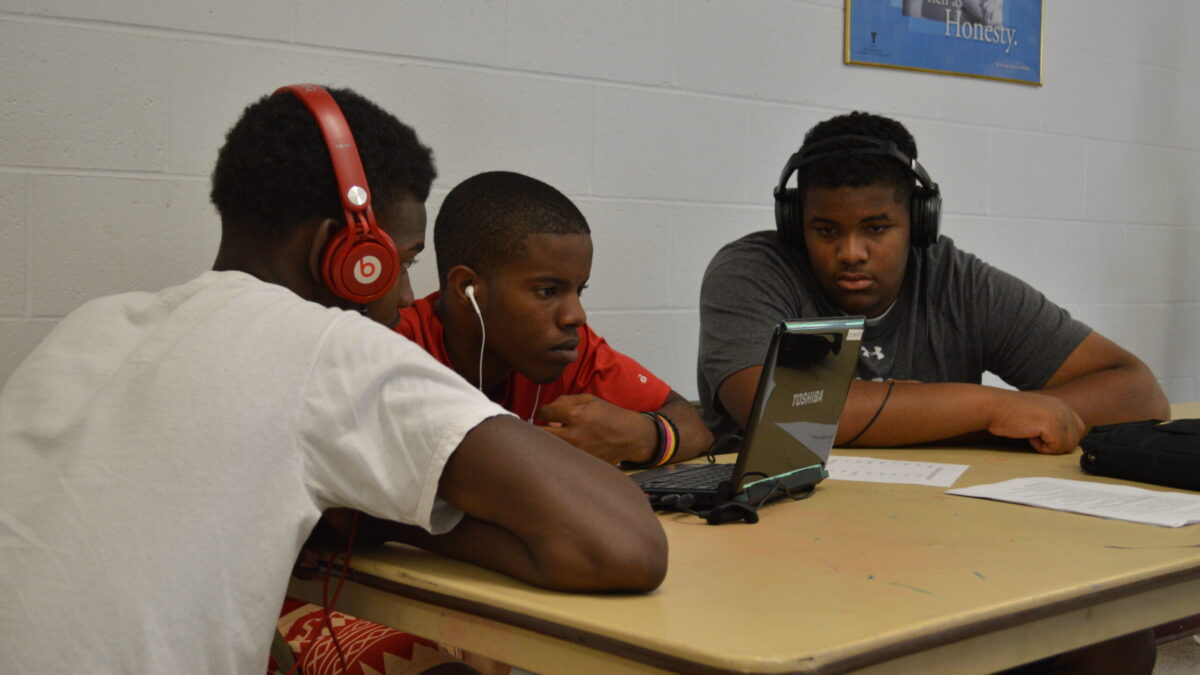 Three youth wearing headphones looking at a laptop computer