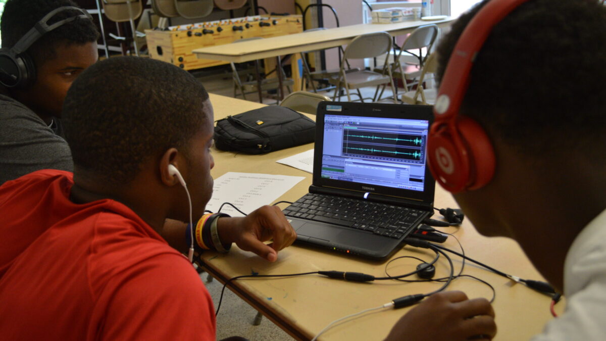 Three youth wearing headphones looking at a laptop computer