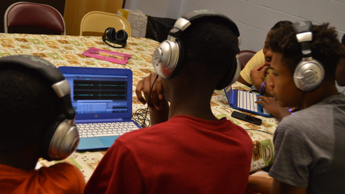 Three youth wearing headphones looking at a laptop computer