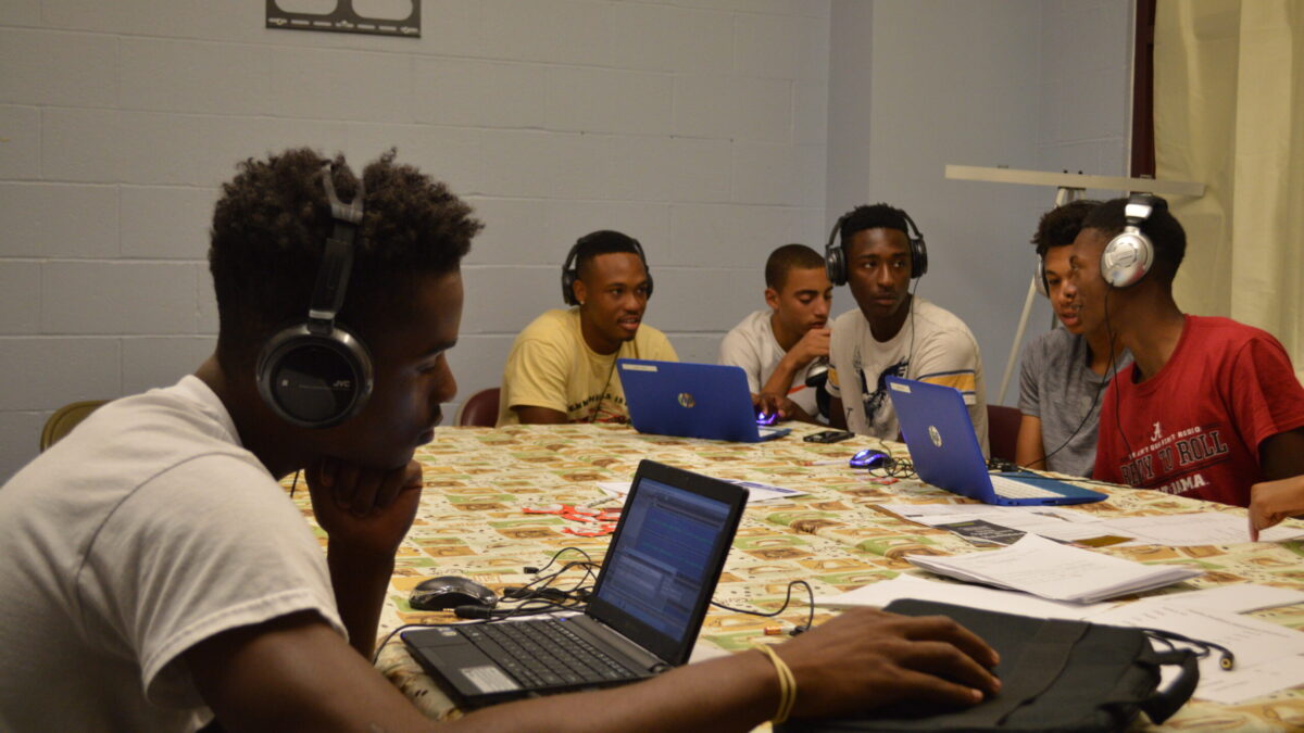 Five youth wearing headphones looking at laptop computers