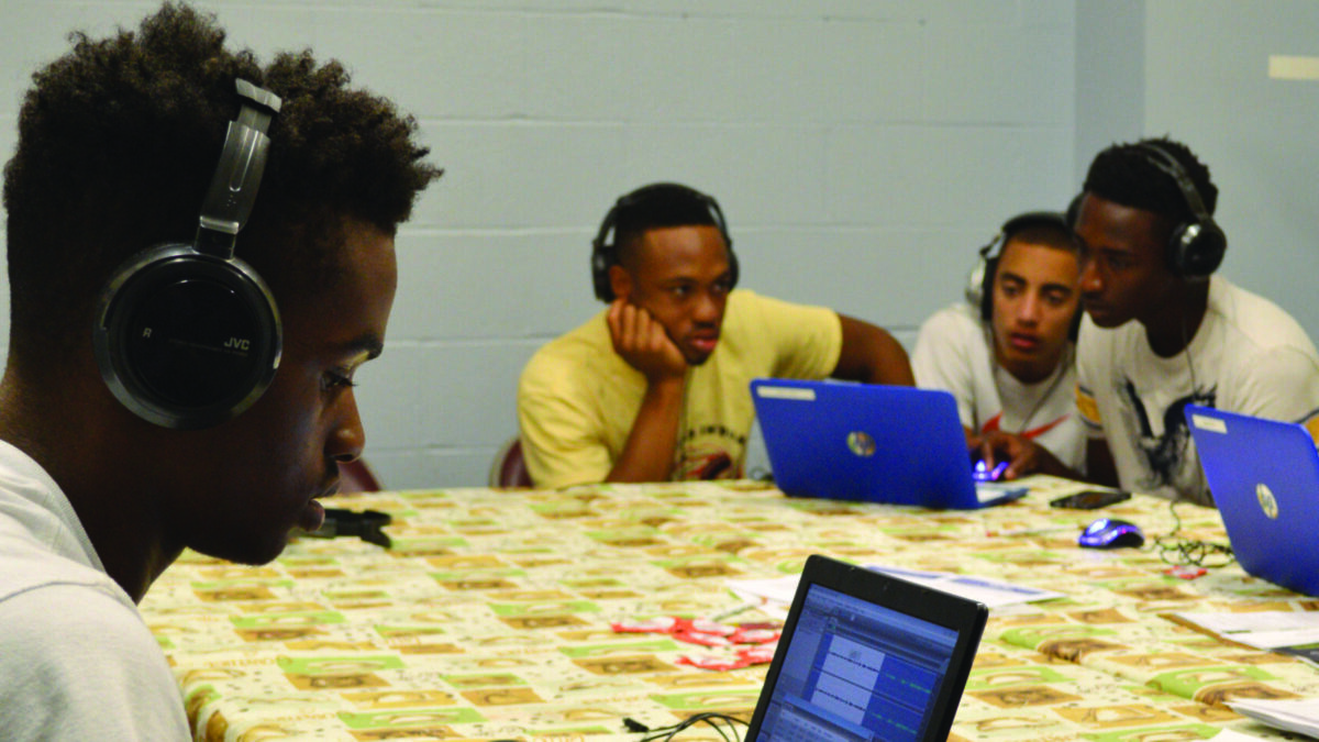 Four youth wearing headphones looking at laptop computers