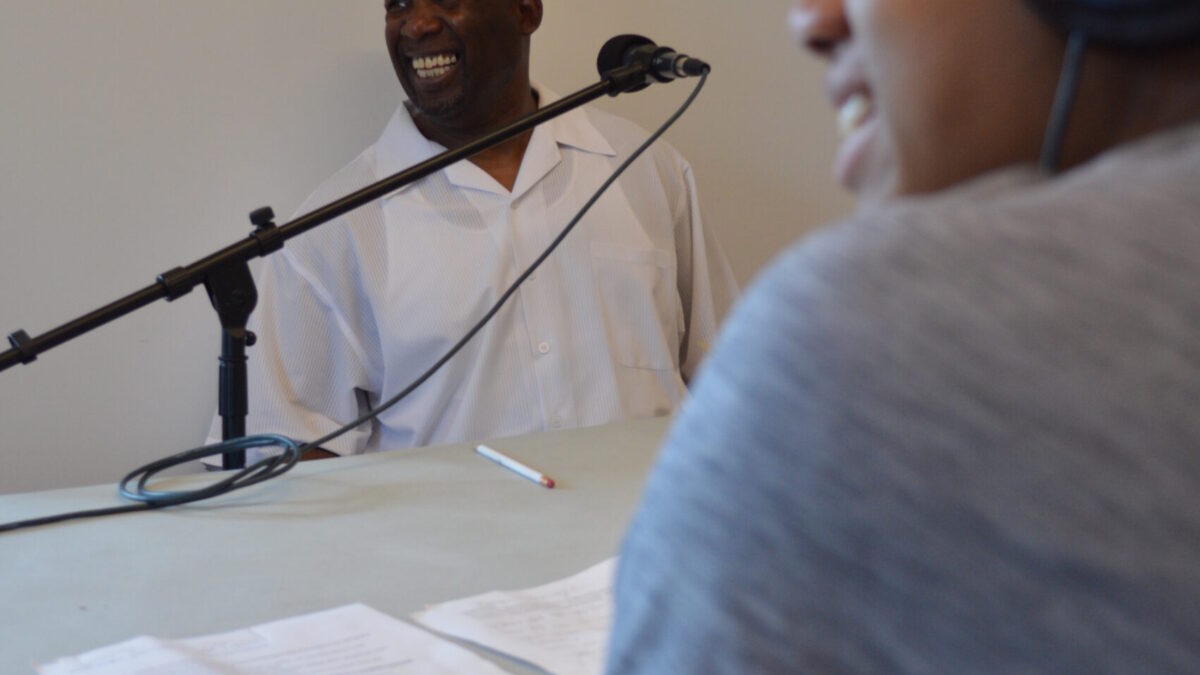A youth wearing headphones interviewing an adult speaking into a microphone.