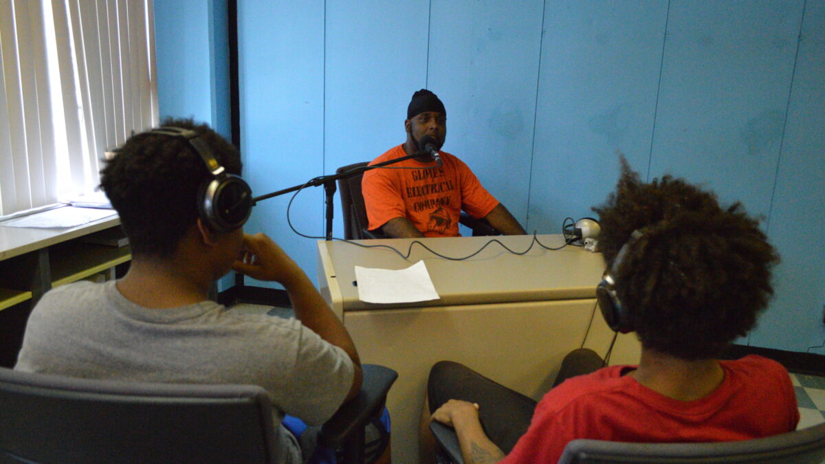 Two youth wearing headphones interviewing an adult speaking into a microphone