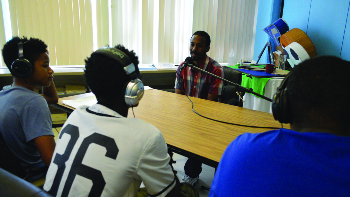 Three youth wearing headphones interviewing an adult speaking into a microphone