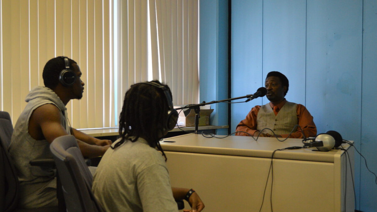 Two youth wearing headphones interviewing an adult speaking into a microphone