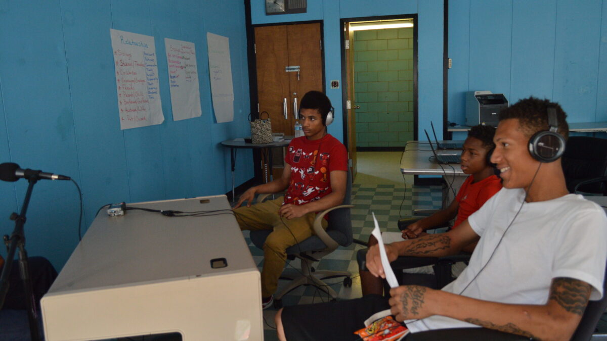 Three youth wearing headphones interviewing an individual speaking into a microphone