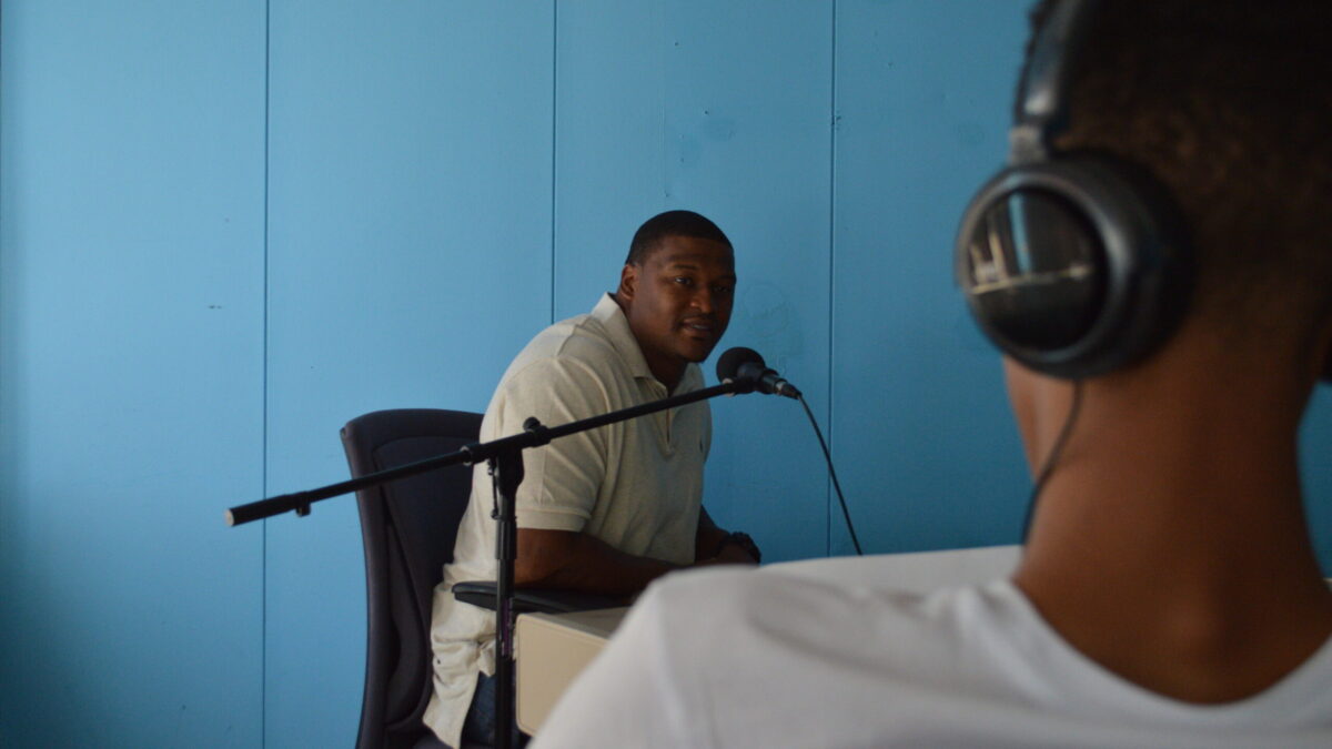 One youth wearing headphones interviewing an adult speaking into a microphone