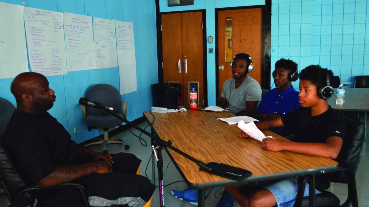 Three youth wearing headphones interviewing an adult speaking into a microphone