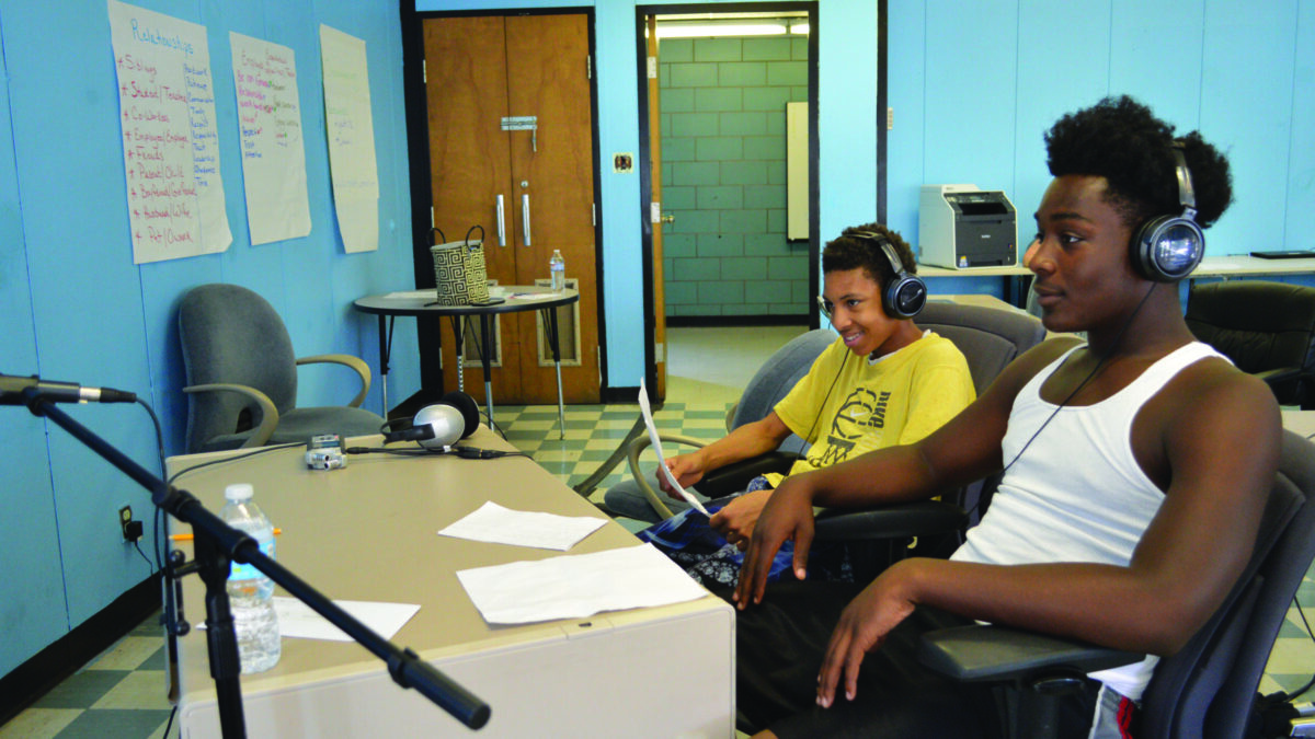Two youth wearing headphones interviewing an individual speaking into a microphone