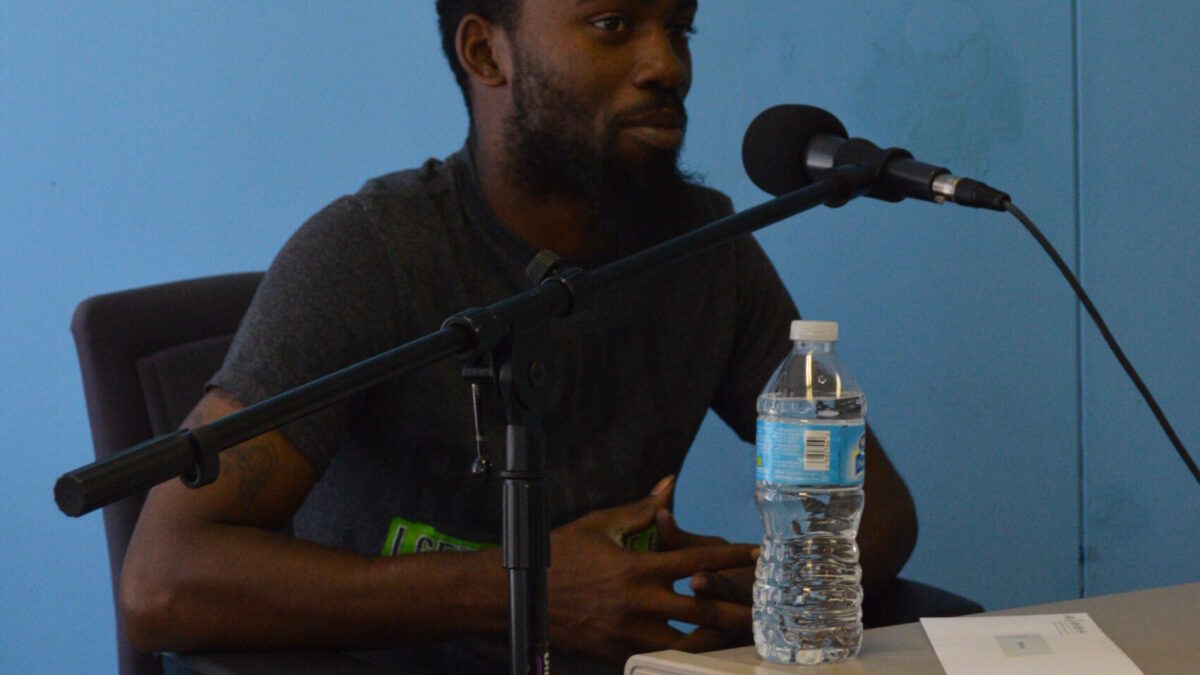 An adult speaking into a microphone in a blue room