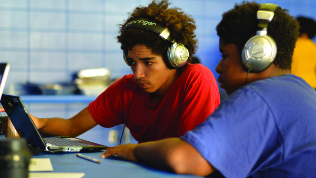 Two youth wearing headphones looking at a laptop computer