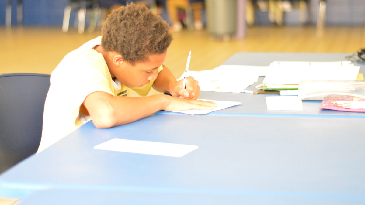 A youth writing on a piece of paper on a light blue table