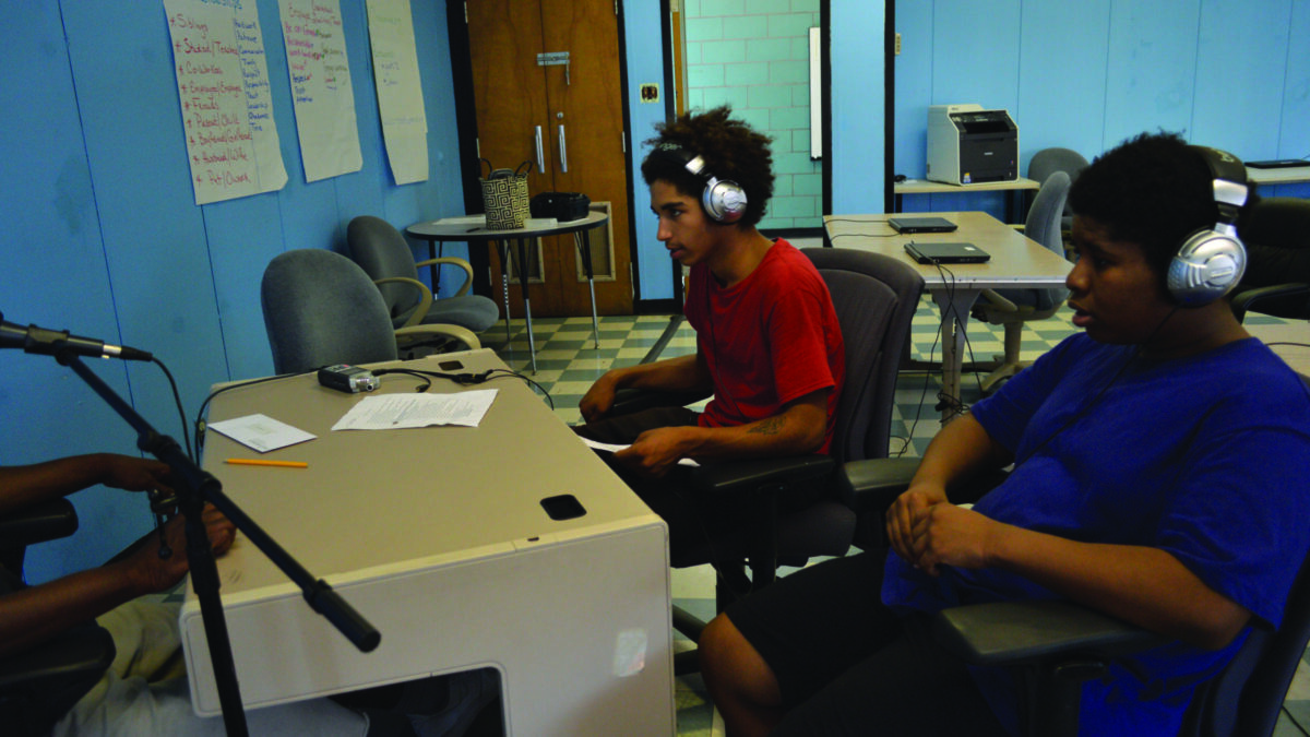 Two youth wearing headphones interviewing an individual speaking into a microphone