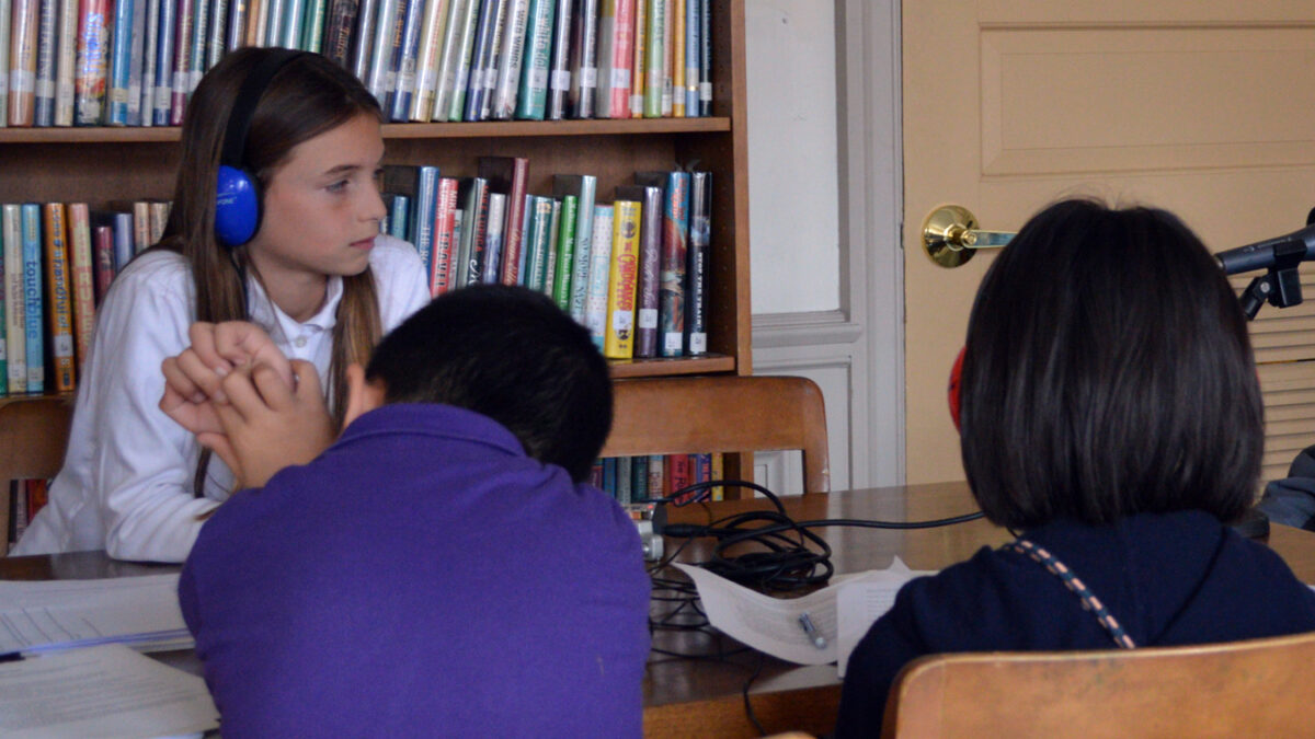 A youth wearing headphones sitting across from two individuals in a library
