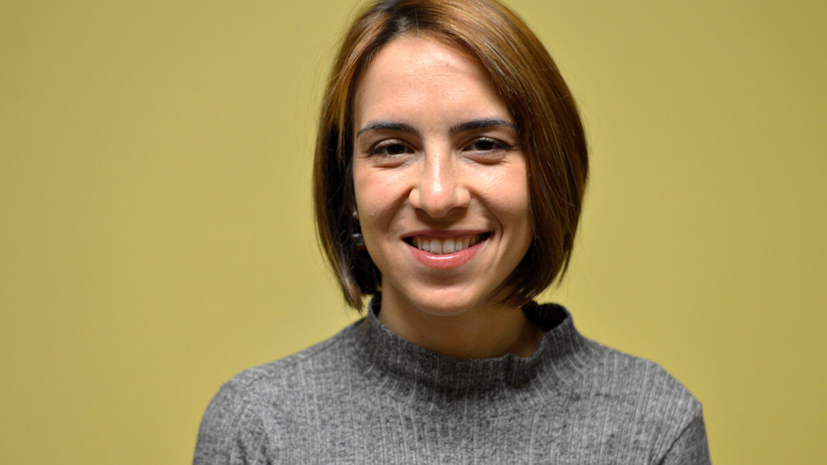 An adult wearing a gray sweater smiling in profile