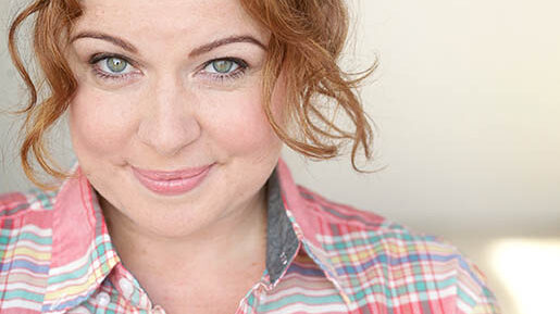 An adult smiling in profile in a white room