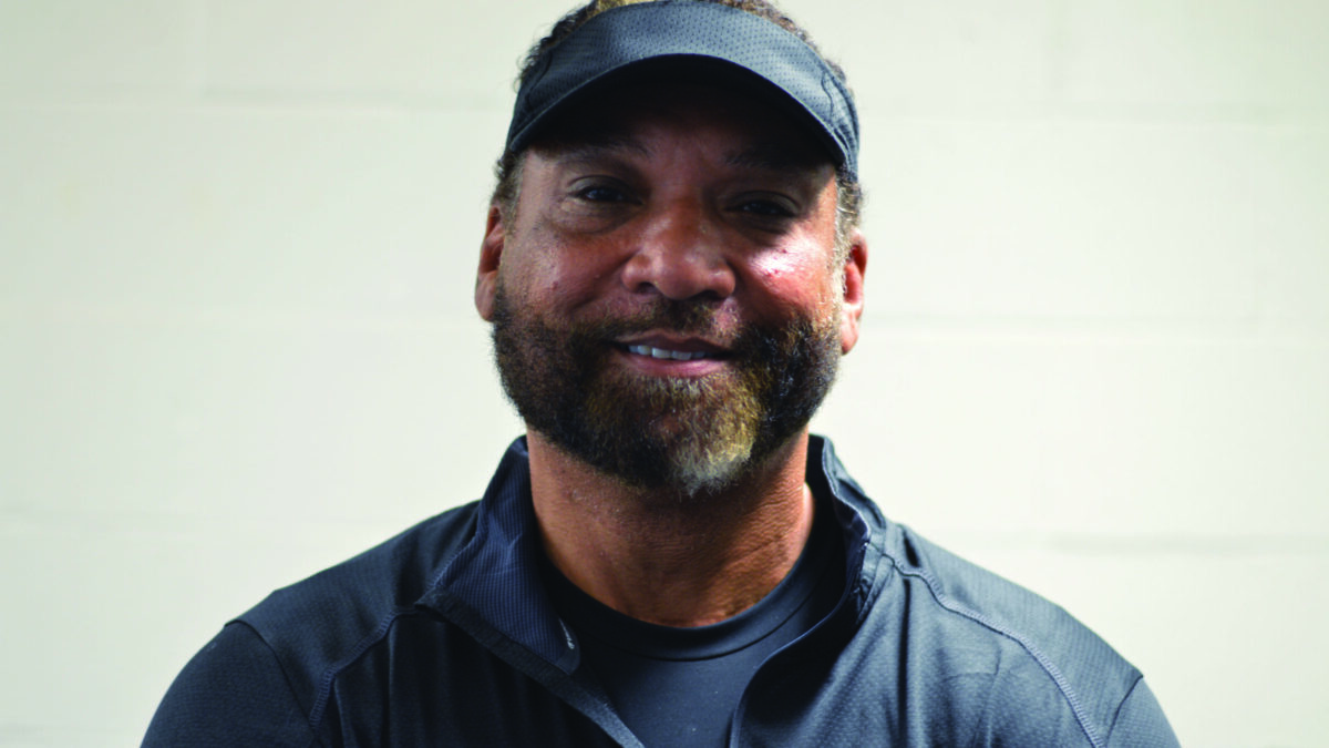 An adult wearing a dark blue shirt and a ballcap smiling in profile