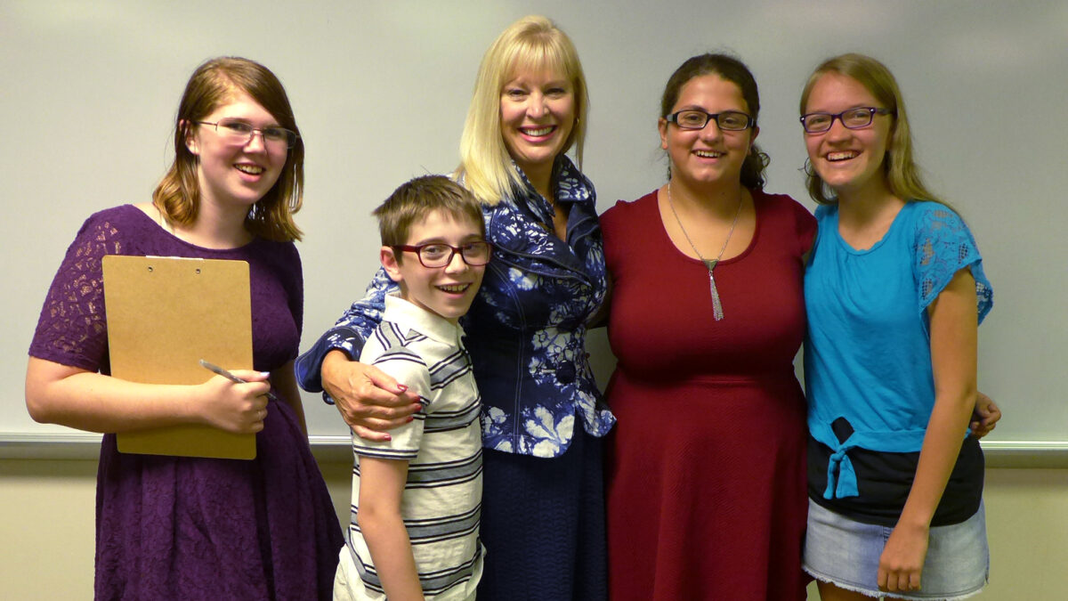 Four adults and a youth smiling and posing in front of a whiteboard