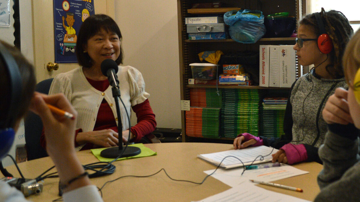 Three youth wearing headphones interviewing an adult speaking into a microphone
